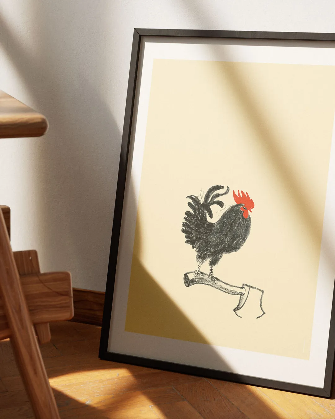 Ein Plakat mit einer Bleistiftzeichnung eines schwarzen Gockels, der auf einem Beil sitzt… und überlebt hat.